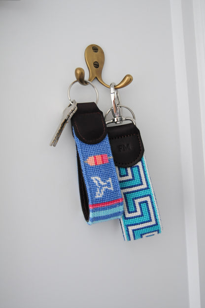 Needlepoint keychains designed by Frances Mary with colorful design hanging on a brass hook.